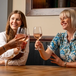 Three women sitting at an indoor table, raising glasses of rose wine in a cheers motion.