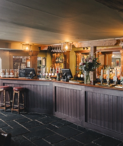 The wood panelled bar inside Ye Olde Swan in Thames Ditton, with stone floor, bar stool seating, and wooden beams.