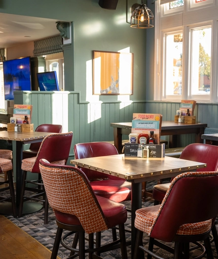 The interior restaurant seating area at the Green Posts in Portsmouth, with a TV on the wall, and upholstered seating.