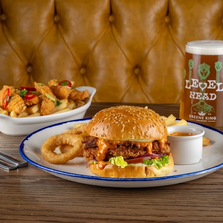 A roasting dish with fries and a plated burger next to a pint of Level Head on a table.