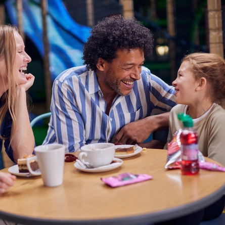 A family enjoying cake and hot drinks at a table in a Wacky Warehouse.