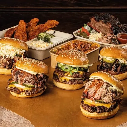 Various burgers and other dishes in takeaway boxes on a wooden table.