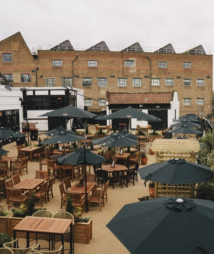 An aerial view of the exterior beer garden seating area at Ye Olde Swan, with wooden furniture, shade umbrellas, string lights, and a view of the waterside.