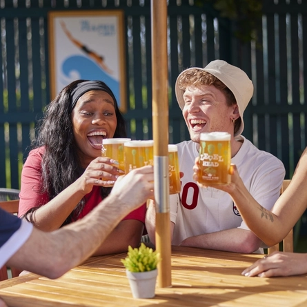 A mixed group of people seated at an outdoor table holding drinks.