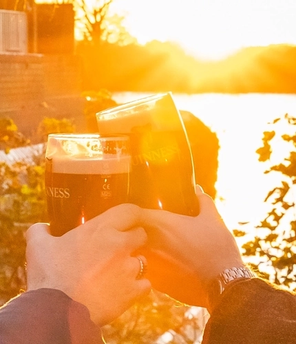 An image of 2 friends with drinks sat at a table within the exterior beer garden seating area with waterside view celebrating with a cheers at The Crabtree.