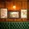 A close up view of framed artwork on a wood panelled wall inside The Plough. A green, upholstered booth seat is visible below the pictures.
