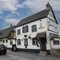 The exterior facade and signage of The Royal Oak in Bishops Cleeve; with a thatched roof, and flower baskets hanging on the walls.