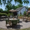 The paved exterior beer garden seating area at The Rising Sun in Wistaston, with shade umbrellas on some of the tables, a wooden planter box filled with plants and flowers, and string lights overhead.
