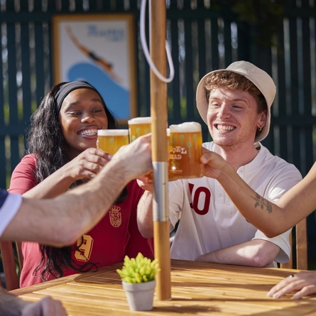 A mixed group of people seated at an outdoor table holding drinks.