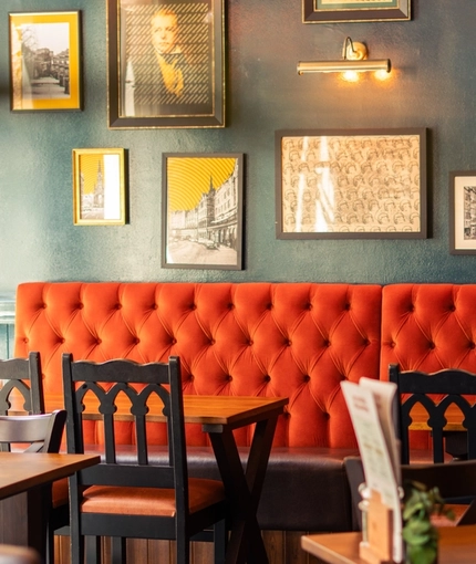 The interior restaurant seating area of The Advocate, with upholstered booth seating, wooden tables, framed artwork on the walls and a TV.