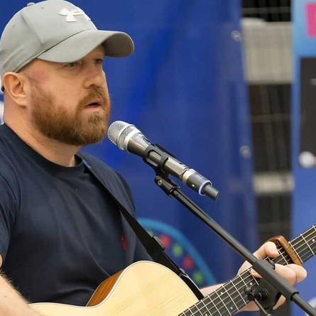 A image of a performer outside with a microphone infront of him playing the guitar, used to advertise 'whats on' in Crafted venues.