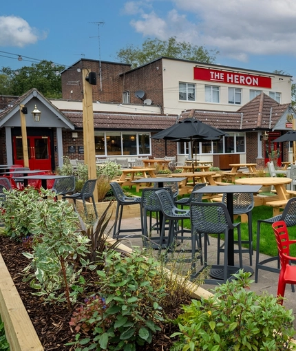The exterior beer garden seating area at The Heron in Havant; with wooden picnic tables, shade umbrellas, and string lights overhead.