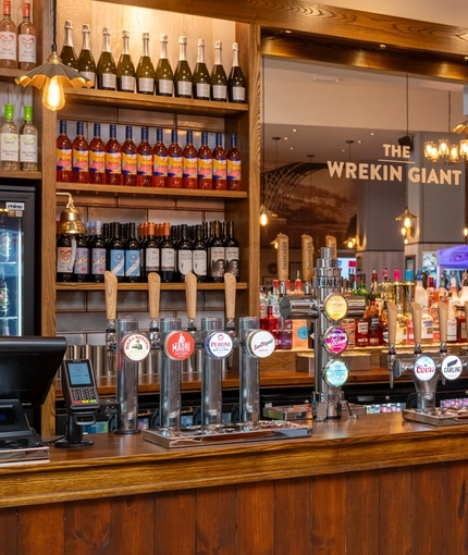 A close up view of the bar inside The Wrekin Giant in Telford, with bottles of wine and alcoholic spirits on wooden shelves behind the counter.