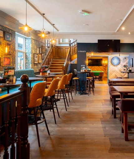 The interior restaurant seating area at The Talbot in Worcester; with a pool table, an illuminated dartboard, TVs on the walls, and a wooden staircase leading to the upper floor.