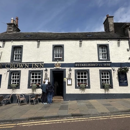 The exterior facade of the venue with hanging baskets and outdoor seating tables and chairs at The Crown Inn.