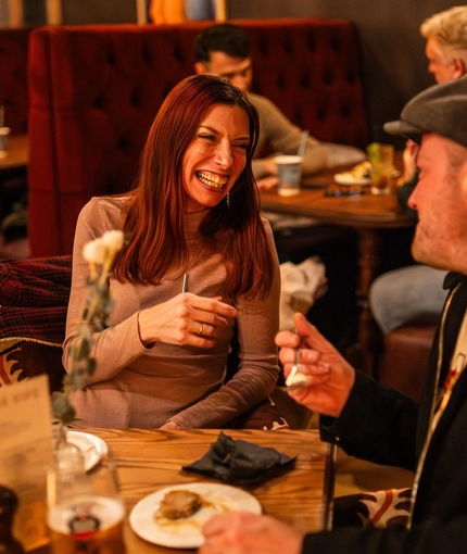 An image focusing on 2 people sat at a table within the interior restaurant seating area enjoying food and drinks at The Black Swan.