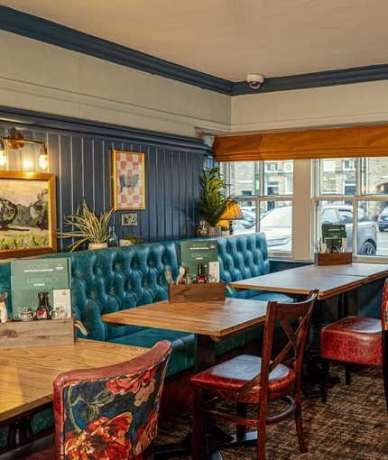 An interior restaurant seating area at The Red Lion, with upholstered chairs and booth seat, and framed artwork on the walls.