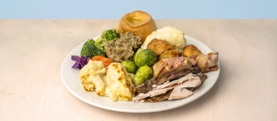 A Carvery dinner featuring slices of roast meat, Yorkshire pudding, mashed potatoes, roast potatoes, Brussels sprouts, broccoli, carrots, cauliflower cheese, pigs in blankets and stuffing, served on a plate.