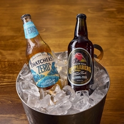 A bottle of Thatchers Zero alcohol cider and a bottle of Koppaberg alcohol free cider sitting in a bucket of ice.