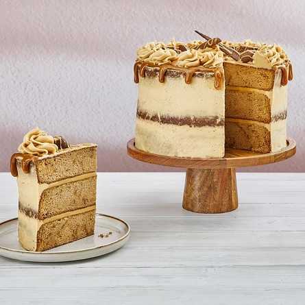 a toffee fudge cake on a stand next to a slice of it on a plate