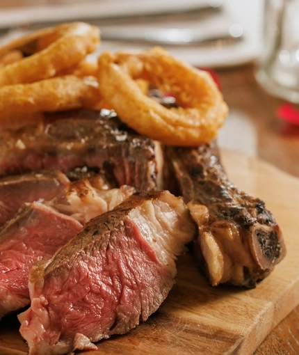 An advertising image of a boarded Ribeye Steak main dish from the Valentines Day menu sat on a table within the interior restaurant seating area at The Crown.
