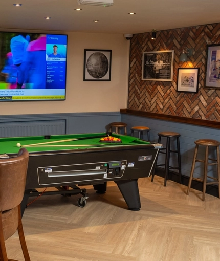 An interior games area at The Cherry Tree in Newcastle-Under-Lyme; with a pool table, a TV on the wall, and restaurant seating.