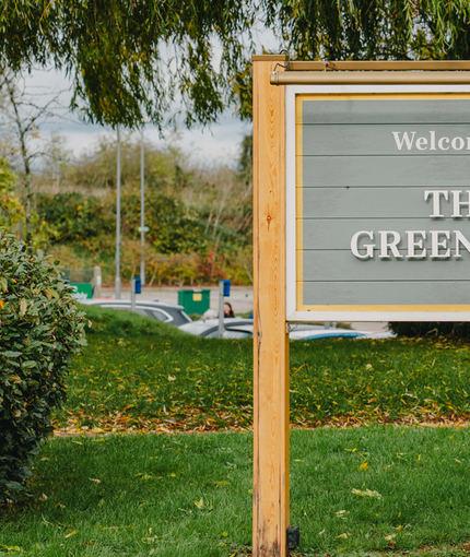 An exterior sign saying "Welcome to The Green Man", which stands on a patch of grass, surrounded by bushes.