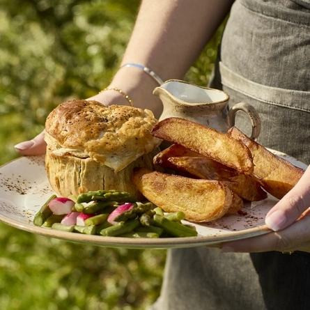 Hands holding a plate of pie, potato wedges and vegetables.