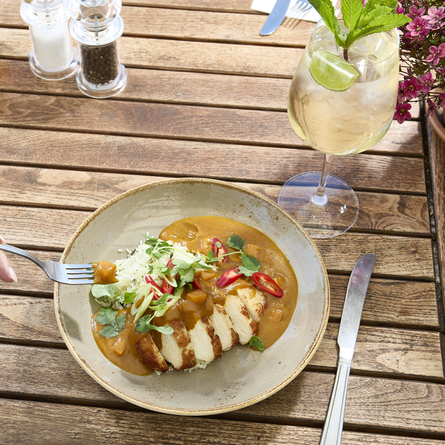 A lifestyle image showing a person sat at a table within the exterior beer garden seating area enjoying a main dish and drinks at a Chef & Brewer venue.