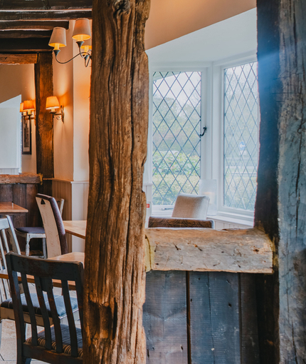 The interior restaurant seating area at The Green Man, with wooden beams on the walls and ceiling, and a fireplace.
