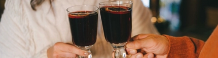 Two people in a pub bar area, holding glasses of mulled wine garnished with orange slices.
