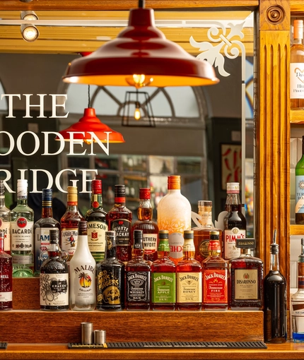 A close up view of bottles of spirits on a wooden shelf at the bar inside the Wooden Bridge.