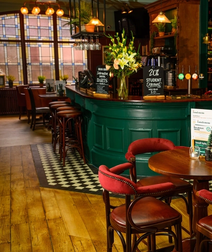 A close up view of two restaurant tables in front of the wood panelled bar of The Globe; with wood flooring, bar stools at the counter, and a TV on the wall in the background.