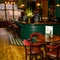 A close up view of two restaurant tables in front of the wood panelled bar of The Globe; with wood flooring, bar stools at the counter, and a TV on the wall in the background.