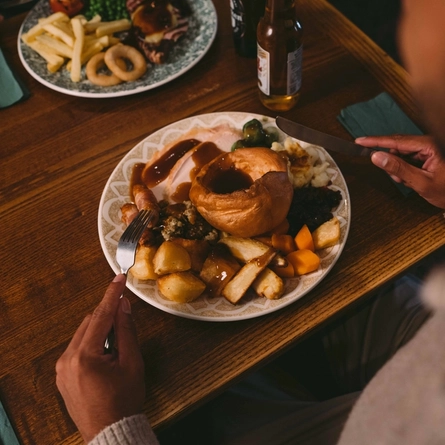 The hands of a person holding cutlery above a plated meal on a festive decorated wooden table.