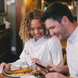 A man and a woman seated at a wooden table enjoying a meal.