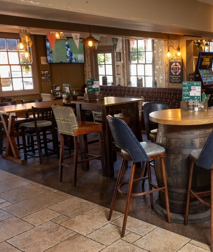 The interior restaurant seating area at The Woolpack Inn in Norwich; with upholstered bar stools, benches, and booth seating; TVs on the walls; a gaming machine; and a fireplace.