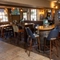 The interior restaurant seating area at The Woolpack Inn in Norwich; with upholstered bar stools, benches, and booth seating; TVs on the walls; a gaming machine; and a fireplace.