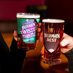 A close up view of two hands, one holding a glass of Belhaven Twisted Thistle, and the other holding a glass of Belhaven Best.