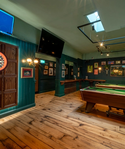 The interior games area at the Lord Raglan, with wooden floor, pool tables, a dartboard, and TVs on the wall.
