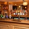 A close up view of the wood panelled bar inside the Ye Olde Leathern Bottel in Barkham, with spherical glass lights hanging above the counter, and bottles of wine and alcoholic spirits on wooden shelves behind the bar.