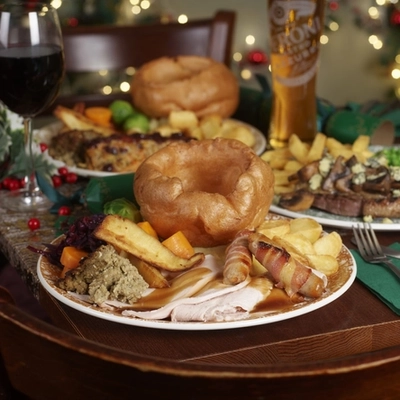 An advertising image focusing on a Turkey Dinner Carvery dish with various plated Festive Main dishes in the background and a selection of drinks available at a Pub & Carvery venue.