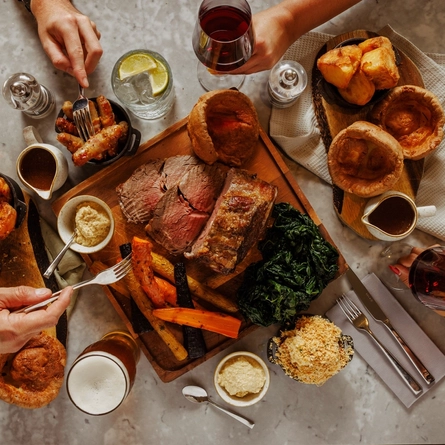 An image of a people enjoying a Sunday Roast sharing platter dish with sides and a selection of drinks within the interior restaurant seating area at The Foundry Bell.