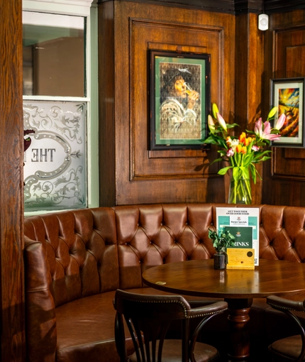 An interior restaurant seating area at The Plough in Bloomsbury, with a semi-circular upholstered booth seat, and framed artwork on the wood panelled walls.