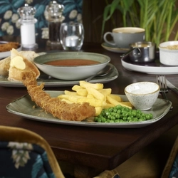 A wooden indoor table holding a plate of Fish & Chips, with other plated meals and drinks.