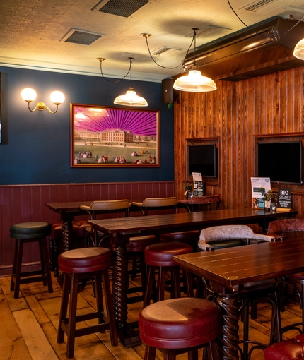 An interior restaurant seating area at the Phoenix; with padded bar stools and bench seating, and three TVs on the wood panelled wall.