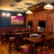 An interior restaurant seating area at the Phoenix; with padded bar stools and bench seating, and three TVs on the wood panelled wall.