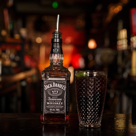 A bottle of Jack Daniels next to a glass of Jack Daniels & Coca-Cola on a bar.