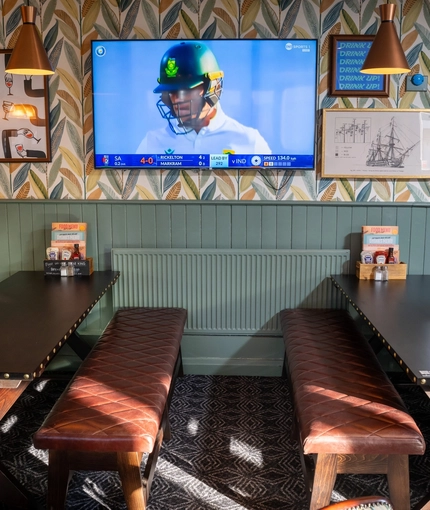 An interior restaurant seating area at the Green Posts, with a TV on the wall, and upholstered bench seating.