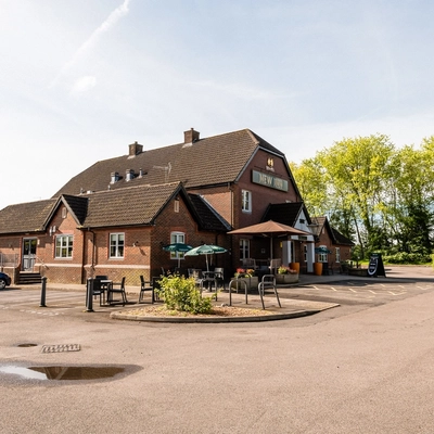 Exterior facade of a pub with a seating area and a car park.